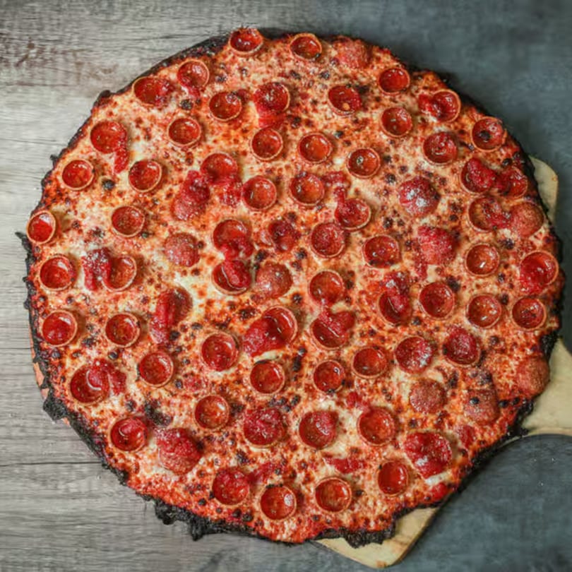A large, round Malatesta's pepperoni pizza with a crispy, slightly charred crust on a wooden peel.