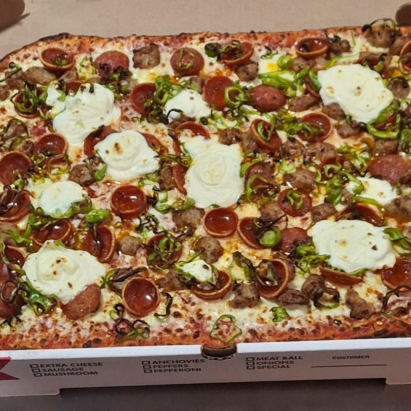 A rectangular Malatesta's pizza with pepperoni, sausage, green peppers, and dollops of ricotta cheese.