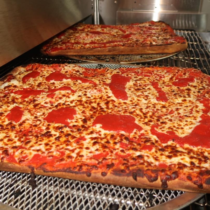 Two rectangular Malatesta's pizzas with melted cheese and dollops of red sauce in an oven.
