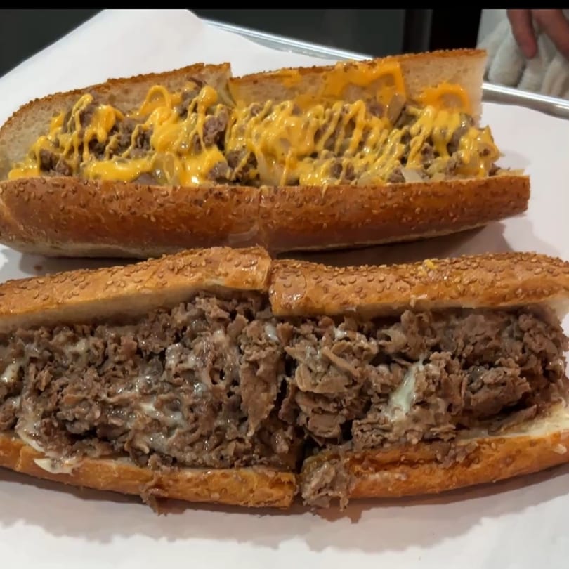 Two Malatesta's cheesesteak sandwiches on sesame seed rolls, one with cheese sauce, the other with white cheese.
